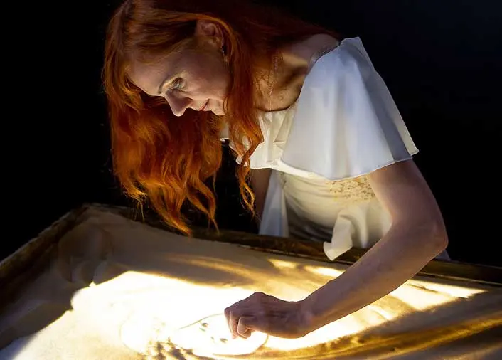 Sand artist Daria Tym drawing a woman's face with sand on a lightbox