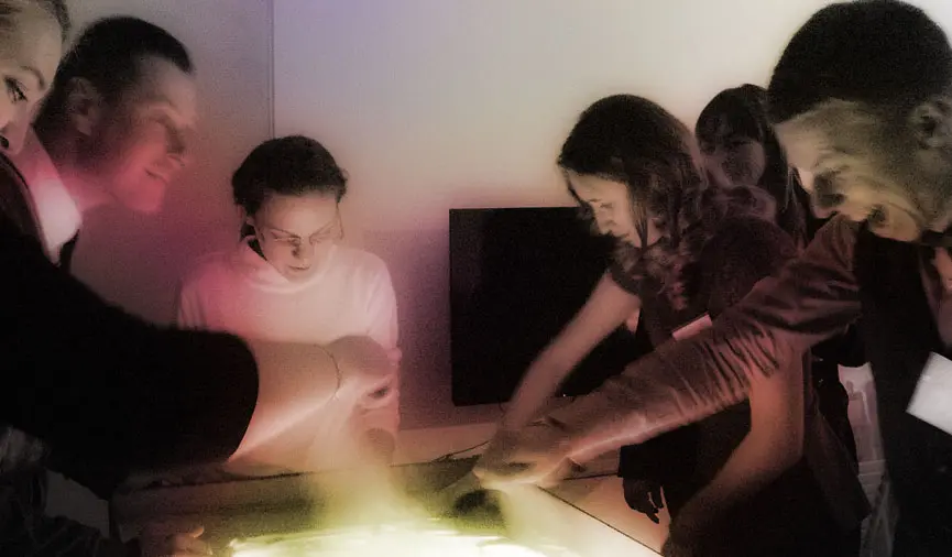 Sand artist leading a sand painting masterclass for a group of adults at a corporate event