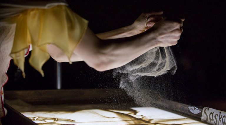 Close-up of an artist's hand creating a live sand show for music concerts during a performance with Lords of the Sound at the Lviv Opera House.