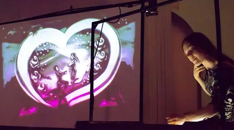 The artist Daria Tym creating a romantic live sand animation painting on an illuminated table during a wedding show performance.